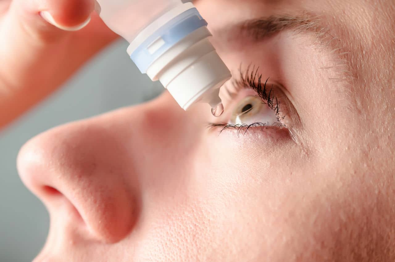 A close up picture of a woman applying eye drops to her left eye